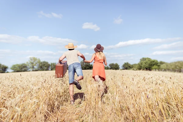 Couple running in field, man holding in his hand vintage suitcase on countryside landscape blue sky outdoors background — Stock Photo, Image