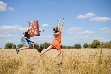 Neşeli genç çift buğday alanında eğleniyor. Retro deri çanta ile açık mavi gökyüzü üzerinde çalışan kadın ve erkek heyecanlı