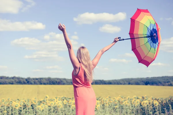 Vedere din spate a frumoasei doamne care deține umbrelă multicoloră în câmp de floarea soarelui și cerul albastru în aer liber . — Fotografie, imagine de stoc