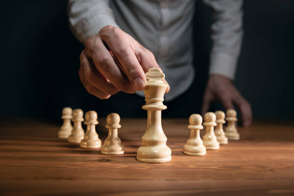 бизнесмен со сложенными руками планирует стратегию с шахматными фигурами на старом деревянном столе.