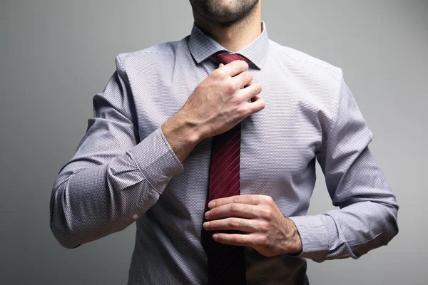 man straightens his tie on a gray background .