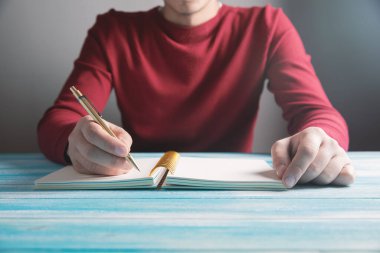 Genç bir adam deftere yazar.