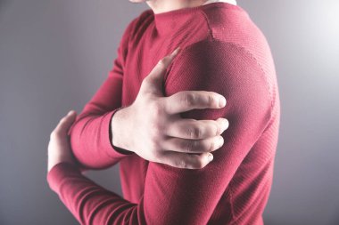 Gri arka planda omzunu ağrıyla tutan genç bir adam.