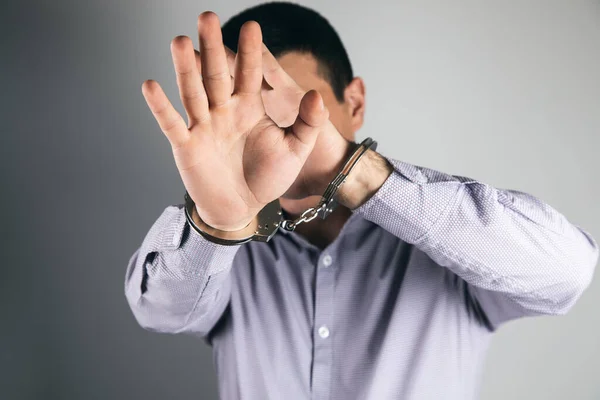 man in handcuffs covers his face