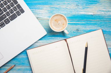 Masada dizüstü bilgisayar, not defteri, kalem ve kahve var.