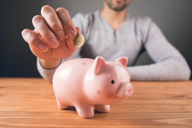 Adamın biri kumbaraya bozuk para koyuyor.