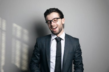 Takım elbiseli ve gözlüklü bir adam gri arka planda gülüyor.