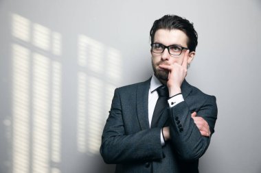 Takım elbiseli ve gözlüklü adam gri arka planda düşünür.