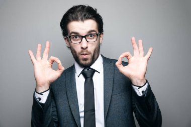 Takım elbiseli ve gözlüklü adam gri arka planda iyi görünüyor.