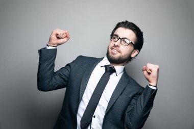 Takım elbiseli ve gözlüklü bir adam gri arka planda keyifle yumruğunu sıktı.