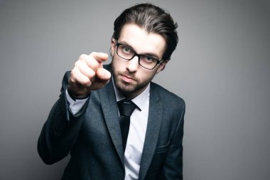 Takım elbiseli ve kızgın gözlüklü adam gri arka planı işaret ediyor.