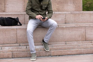 Sokakta genç bir adam telefonda oturuyor.