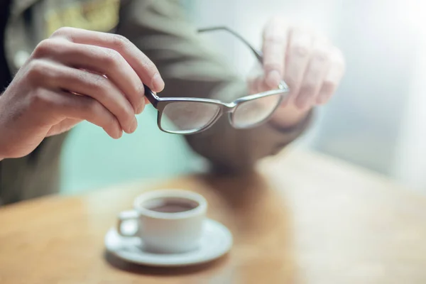 young guy sits in front of coffee and holds glasses