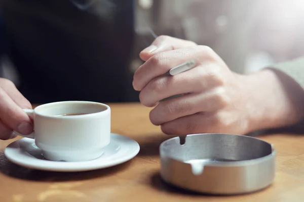 a young guy drinks coffee and smokes a cigarette in a cafe