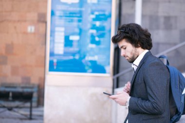 Takım elbiseli, elinde bir çantayla sokakta yürüyor.