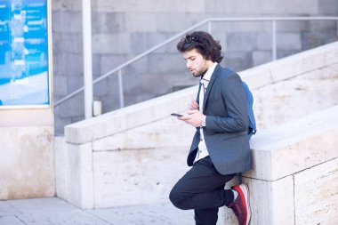 Takım elbiseli, elinde bir çantayla sokakta yürüyor.