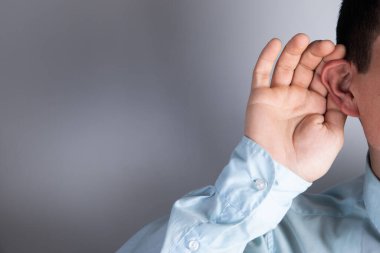 Kulağını çerçeveletti ve gri bir arka planda dinliyor.