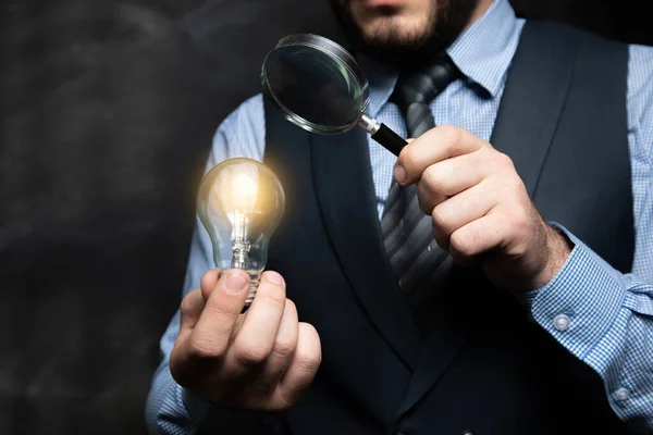 a man looking at a lamp through a magnifying glass on a black background