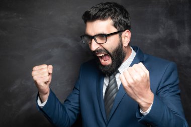 Genç bir iş adamının karanlık bir arka planda zevk için yumruklarını sıkmasının portresi.