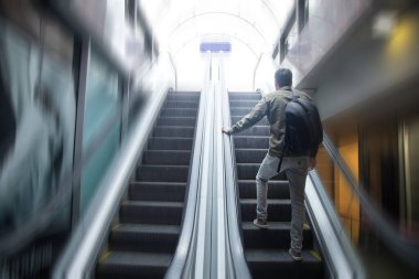 Metronun çelik yürüyen merdiveninde yürüyen bir adam.
