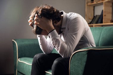 Üzgün bir adam kanepede oturur. koyu renk.