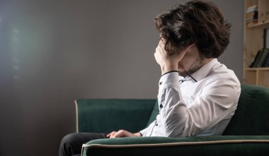 Üzgün bir adam kanepede oturur. koyu renk.