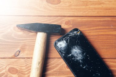 broken smartphone screen and hammer on wooden background