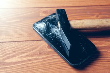 broken smartphone screen and hammer on wooden background