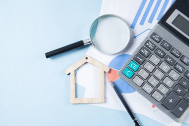 on a blue table a calculator, statistics, a pen and a house
