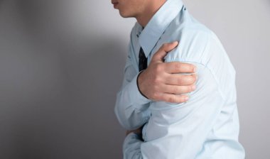 Gri arka planda bir adamın omuz ağrısı vardır.