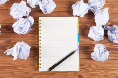 wads of papers on a wooden desktop and a notebook