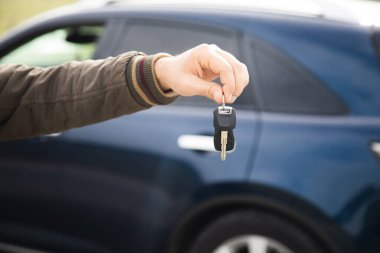 man holding keys on the background of a blue car