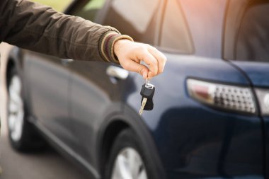 man holding keys on the background of a blue car