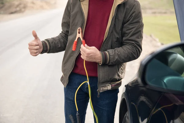 a man stands in front of a car holding a battery jumper