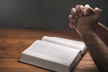 Karanlık bir arka planda kitap üzerinde dua eden bir adam.