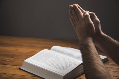 Karanlık bir arka planda kitap üzerinde dua eden bir adam.