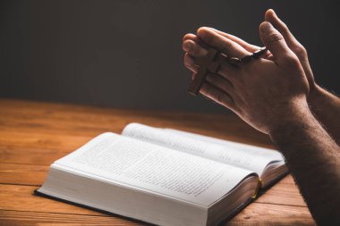 Karanlık bir arka planda kitap üzerinde dua eden bir adam.