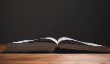 Karanlık bir arka planda, tahta bir masada açık bir kitap.