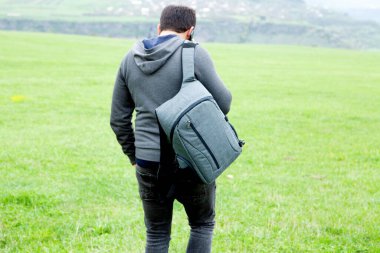 Sırt çantalı bir adam akşam yeşil bir tarlada yürüyor.