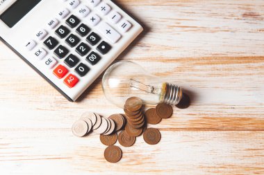 Hesap makinesi, lamba ve paralar ahşap bir masada.