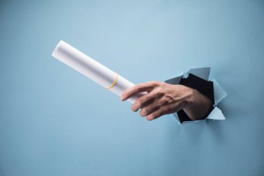 Adamın eli mavi arka planda kağıtları tutuyor.