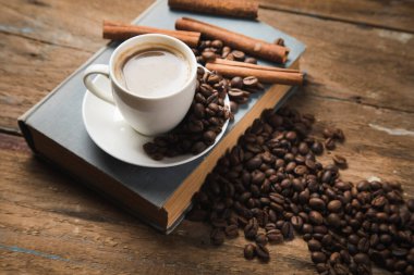 Bir fincan kahve, kahve tohumu, tarçın ve ahşap bir masada bir kitap.