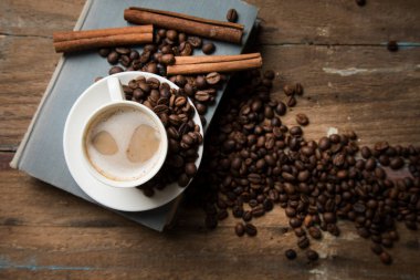 Bir fincan kahve, kahve tohumu, tarçın ve ahşap bir masada bir kitap.