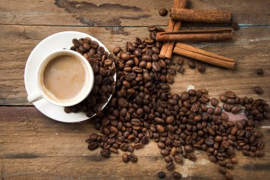 Bir fincan kahve, kahve tohumu, tarçın ve ahşap bir masada bir kitap.