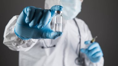 Koruyucu üniformalı bir doktor elinde şırınga ve ampul tutuyor.