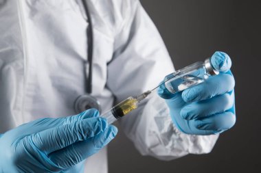 Eldivenli, maskeli ve koruyucu üniformalı bir adam şırıngaya ilaç koyuyor..