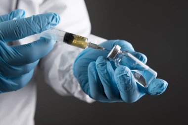 Eldivenli, maskeli ve koruyucu üniformalı bir adam şırıngaya ilaç koyuyor..