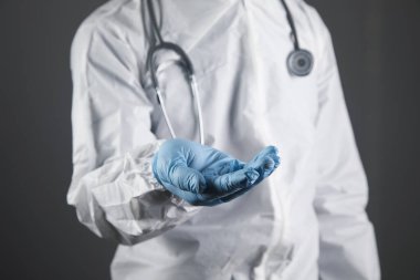 Koruyucu üniformalı doktor avuç içi açık gösteriyor. Eller ayakta duracak şekilde.