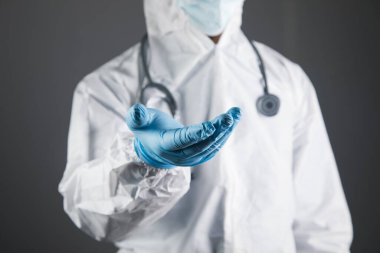 Koruyucu üniformalı doktor avuç içi açık gösteriyor. Eller ayakta duracak şekilde.