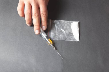 Bir el, üzerinde sıvı olan bir şırıngaya uzanır ve masanın üzerinde bir torba toz vardır. konsept bağımlısı